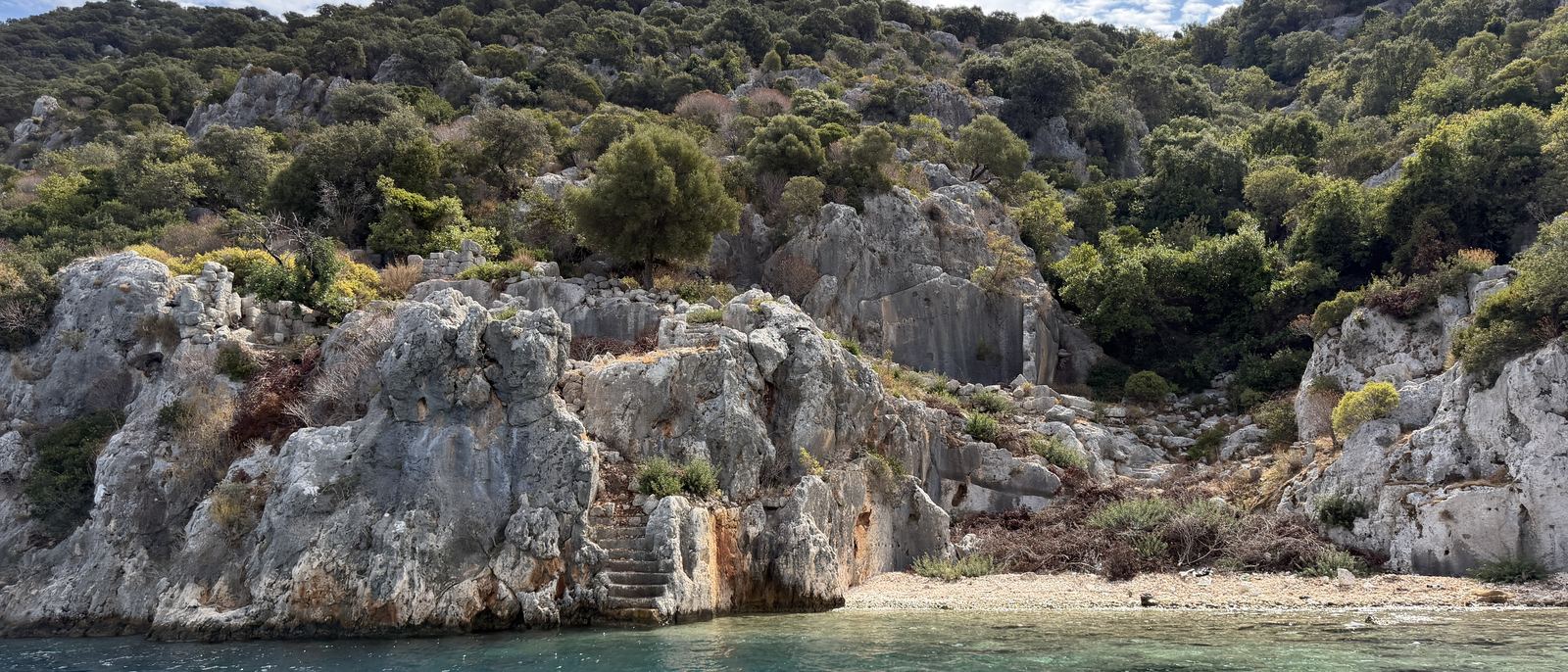 Felsige Küste in Kekova, klares türkisfarbenes Wasser und ein kleiner Kiesstrand