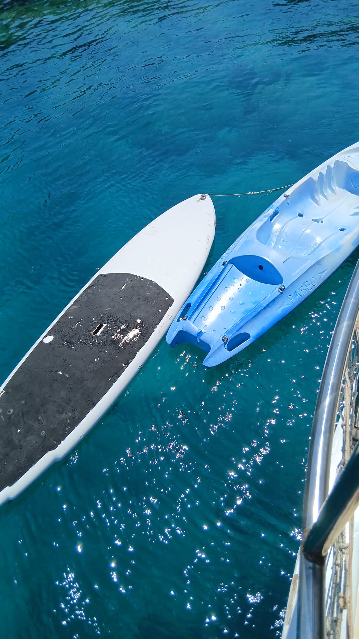 Paddleboard and canoe tied alongside the boat in clear water